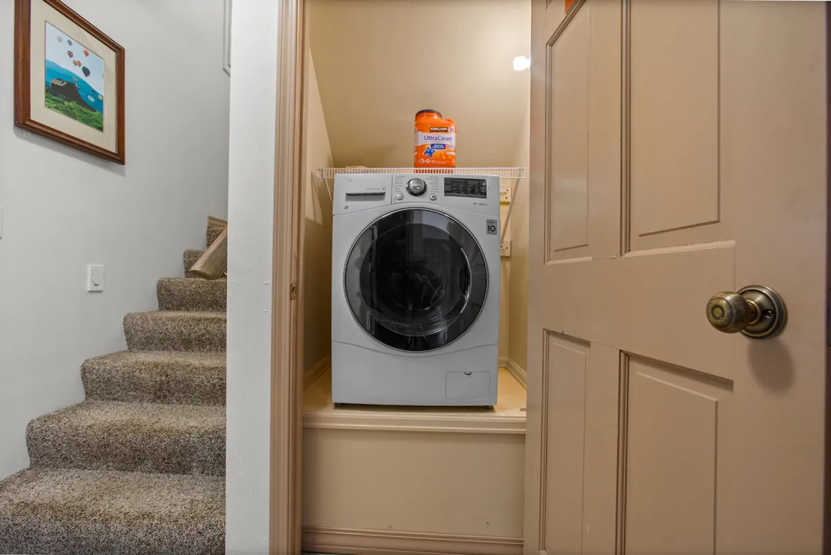 A practical laundry area with a washer and dryer, adjacent to a staircase and cleaning supplies. The space is clean, functional, and designed for the convenience of extended stays, providing everything needed for guests to refresh their gear after outdoor activities.