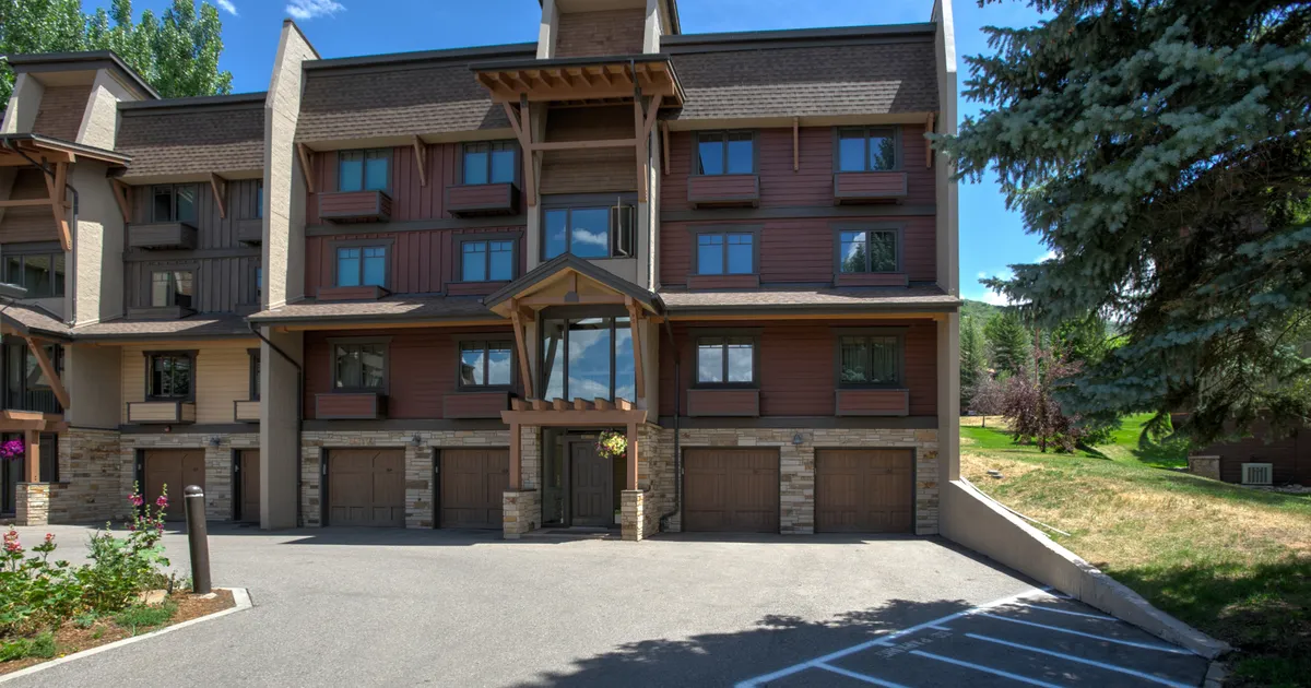The central entrance of the property with a welcoming overhang, detailed stonework at the base, and large windows reflecting the surroundings. The sunlit porch and landscaped garden evoke a sense of arrival and easy access, perfect for families and groups.