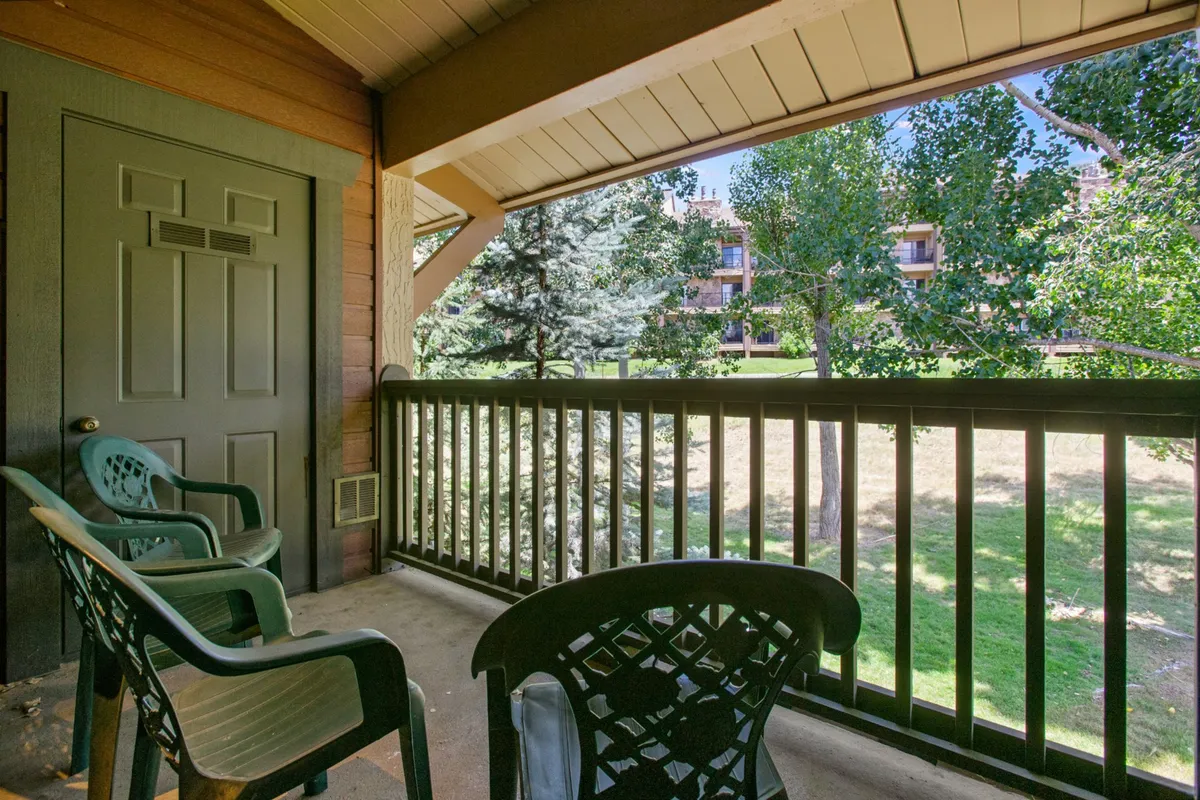 A private balcony with green chairs, a view of trees, and a sturdy railing, offering a peaceful outdoor extension of the living space. The environment suggests fresh mountain air and scenic views, ideal for morning coffee or evening chats.