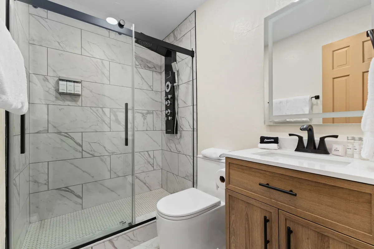A modern and inviting bathroom with a glass shower enclosure, a sleek vanity with sink, and contemporary fixtures. Abundant natural light streams in, creating a refreshing atmosphere ideal for unwinding after a day of activities.