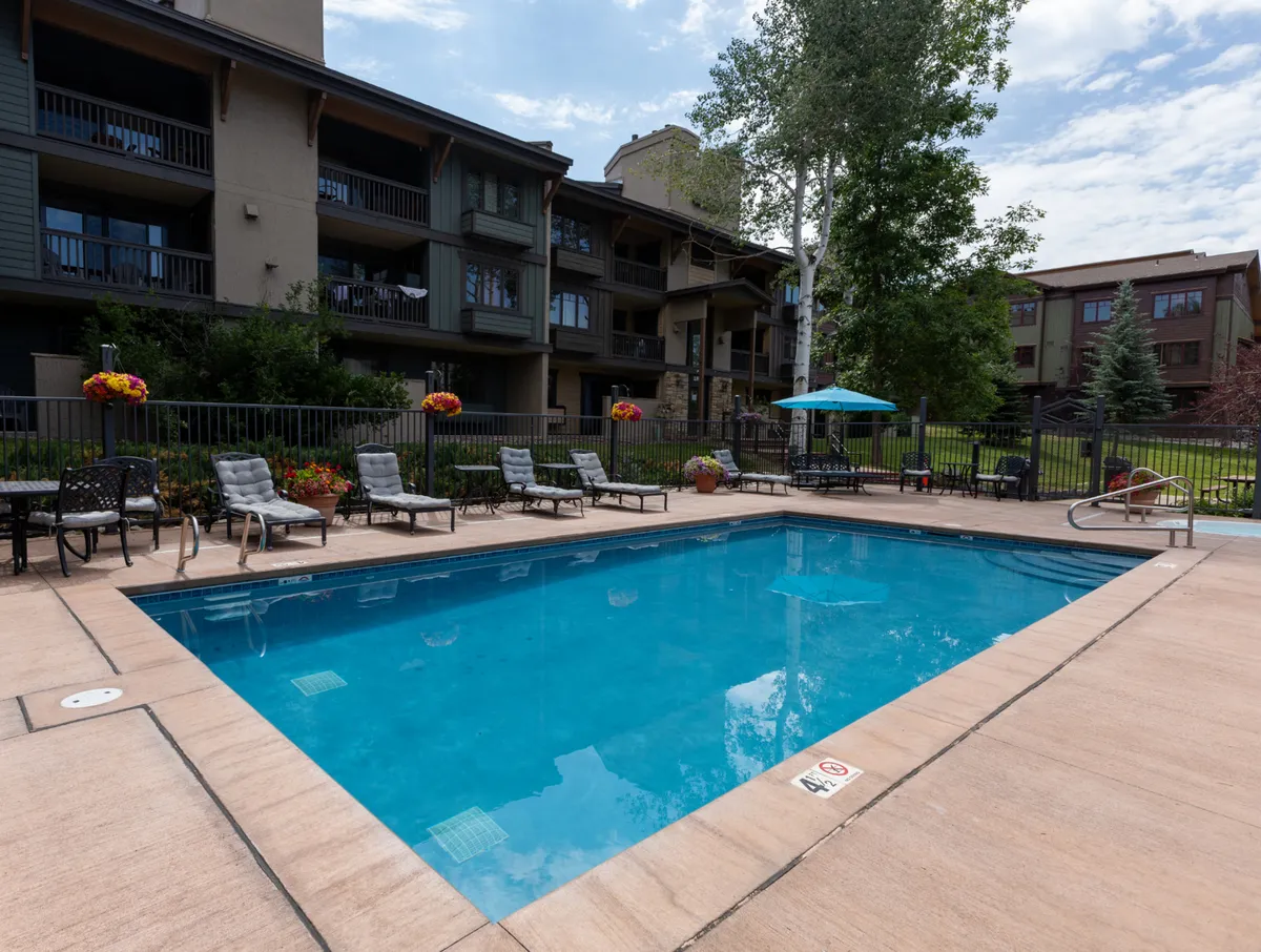 This exterior image features a swimming pool, lounge chairs, lush greenery, and the building’s facade. The mood is inviting and casual, suggesting both relaxation and social opportunities within the community setting.