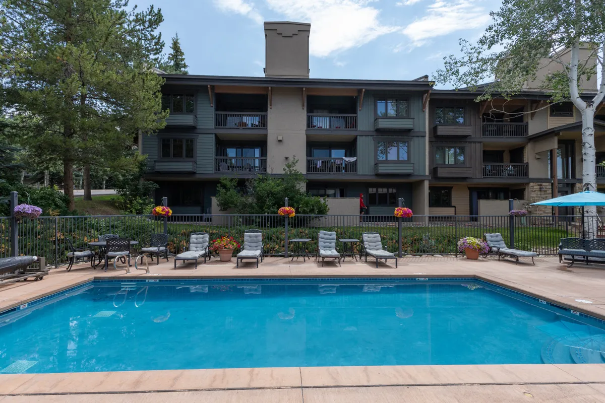 This exterior image showcases the resort's inviting swimming pool area, surrounded by lounge chairs, vibrant flowers, and the facade of the condo building. The relaxed atmosphere and well-maintained landscape highlight the opportunities for refreshing swims and socializing after a day of outdoor activities.