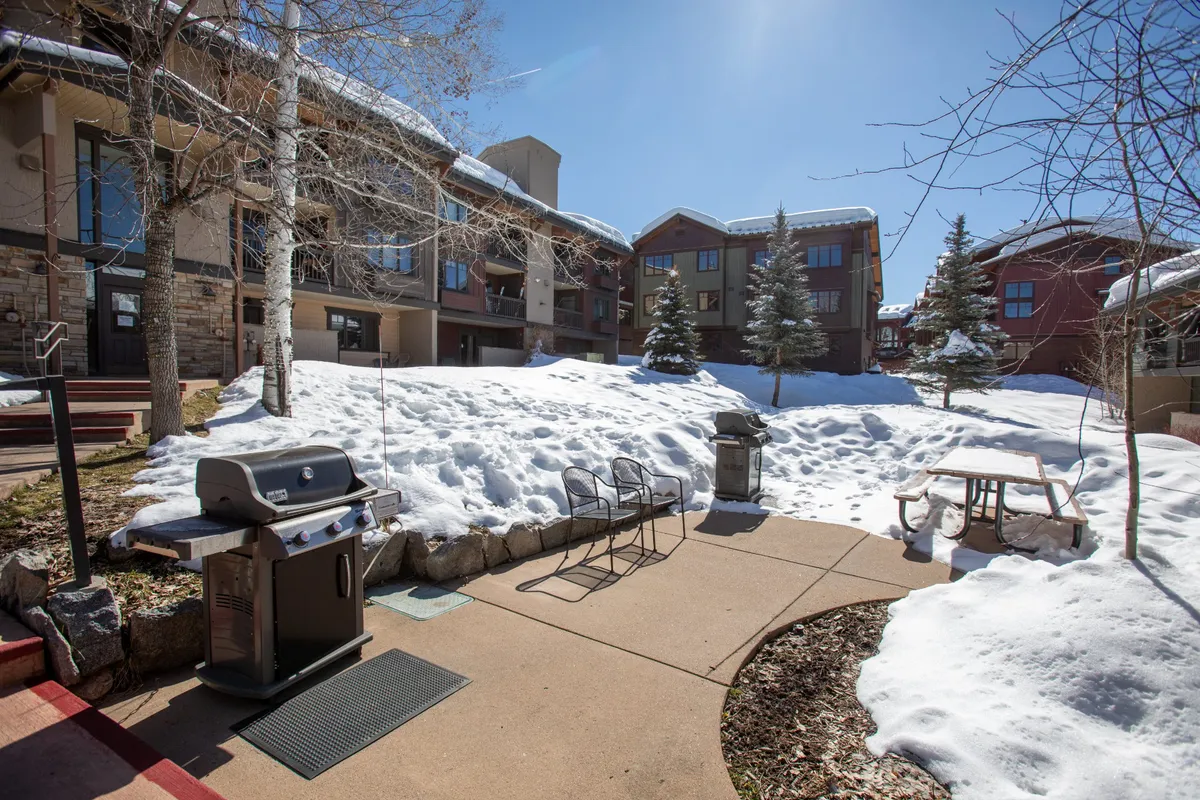 This image showcases an exterior grilling and picnic area, with snow-covered ground and the building's facade visible behind. The scene conveys year-round outdoor enjoyment and the property’s connection to its mountain surroundings.