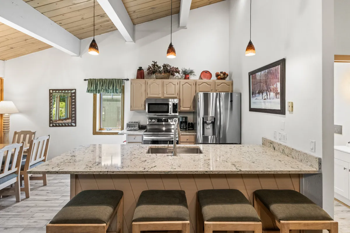 A modern kitchen with a large island, stainless steel appliances, wooden beams, and decorative items. The layout encourages gathering and socializing, while also serving as a practical space to prepare meals after a day of adventure. The kitchen feels warm and inviting, with plenty of room for family activities.